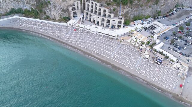 Aerial view of the Crestarella beach with rows of umbrellas, the historic elevator structure, and the hotel perched on the cliff in Vietri sul Mare, Salerno, Campania, Italy.