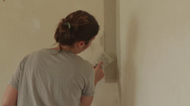 Female contractor leveling drywall surface in room interior