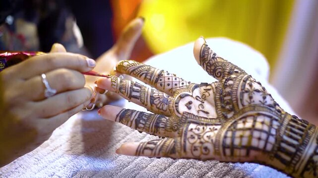 Woman applying intricate mehndi design to hand with bangles on pink fabric, showcasing traditional art. 4K video