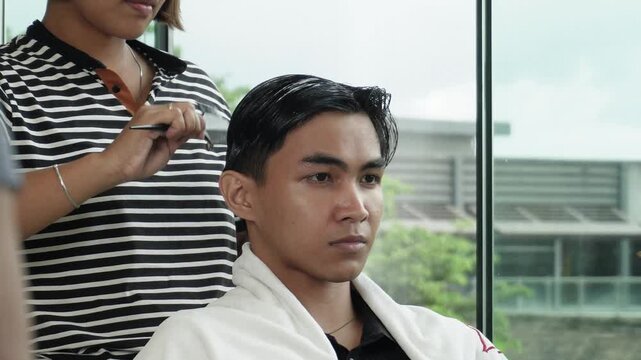 Hair stylist applying protein color cream before professional cellophane hair treatment for Southeast Asian man in his early 20s
