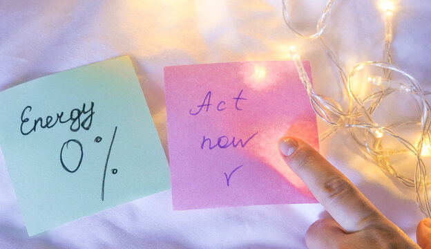 Green and pink sticky notes with messages about zero energy and acting now against a festive holiday light background