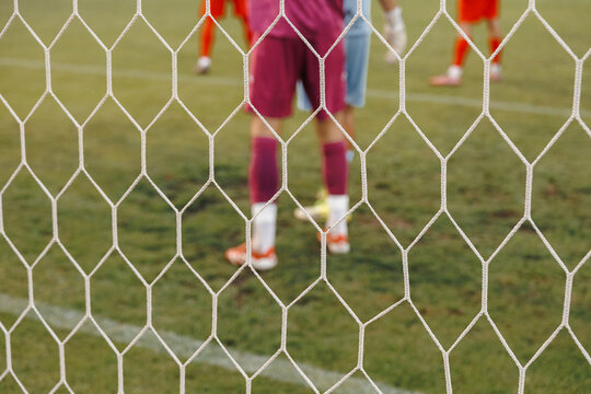 Dynamic soccer action seen through goal net, football ball hitting mesh during match in professional sports stadium competition concept