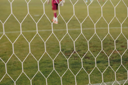 Dynamic soccer action seen through goal net, football ball hitting mesh during match in professional sports stadium competition concept