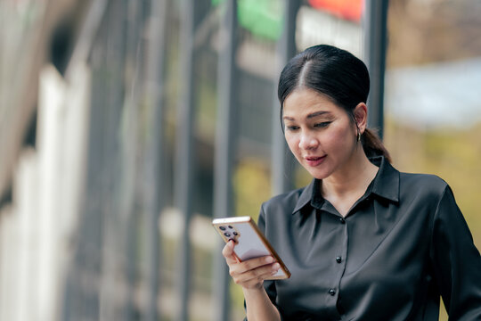 Businesswoman reading business updates on smartphone outside modern office. Professional using mobile technology for communication, task management, online collaboration and digital workflow.