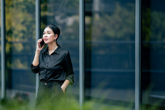 Businesswoman making phone call while standing outside office. Professional using smartphone for business communication, client support, remote collaboration and daily work.