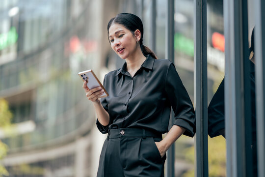 Businesswoman using smartphone for mobile communication outside office building. Professional checking notifications, managing work, staying connected and supporting flexible digital workplace.