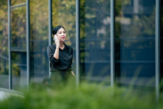 Businesswoman talking on smartphone outside modern office building. Professional handling business communication, client discussion, remote work and mobile technology in corporate environment.