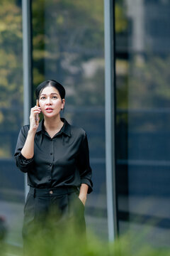 Businesswoman using smartphone for business conversation outside corporate office. Professional communicating with clients, coordinating projects and managing work through mobile technology.