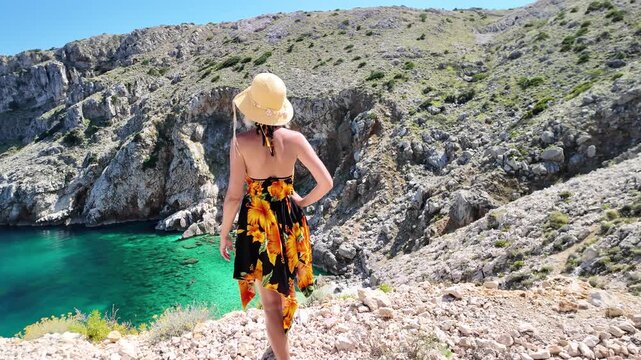 Woman standing on a rocky cliff overlooking Mali Bok beach on Cres Island. Spreading arms wide to embrace warm summer air and stunning turquoise Adriatic sea in Cres Island of Croatia in SLOW-MOTION