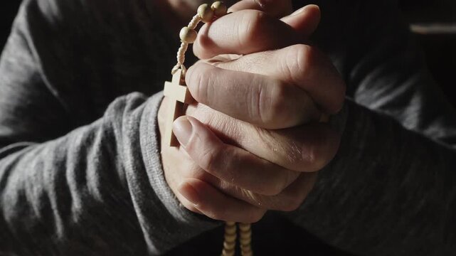 A dramatic close-up of tightly clasped hands holding a crucifix rosary in deep prayer and quiet meditation. Perfect for themes of faith, grief, hope, and spiritual reflection.