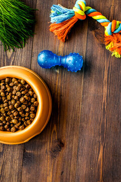 bowl full and overflowing with dry pet - dog food bits and toys on wooden background top view mock-up