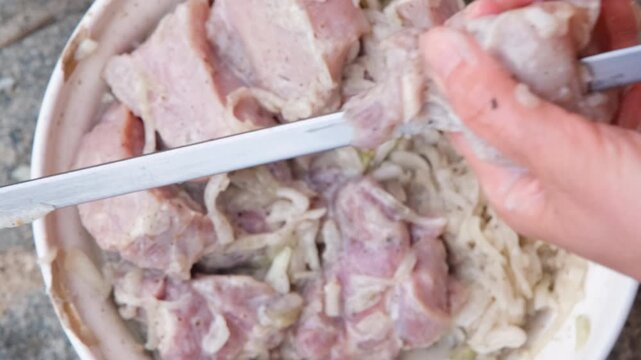 Close-up of hands threading marinated meat onto metal skewers for barbecue, preparing homemade shashlik outdoors with fresh ingredients before grilling over an open fire