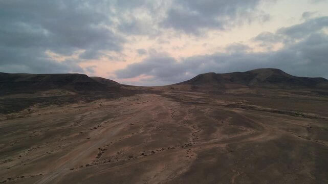 Aerial view of arid volcanic landscape with rolling hills and dramatic cloudy sky in El Cotillo, Canary Islands, Spain.