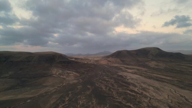Aerial view of arid volcanic hills and rugged terrain under a dramatic cloudy sky in El Cotillo, Canary Islands, Spain.