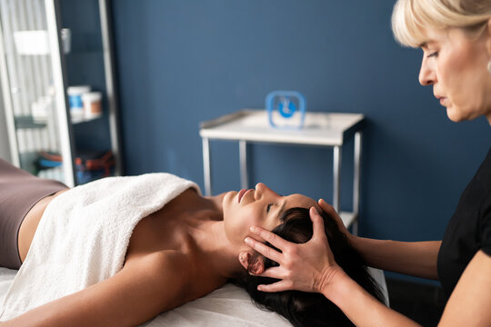 Young woman receiving gentle head massage from therapist in bright treatment room with calm clinical atmosphere and soft natural light, with massage, therapy, therapist, wellness detail