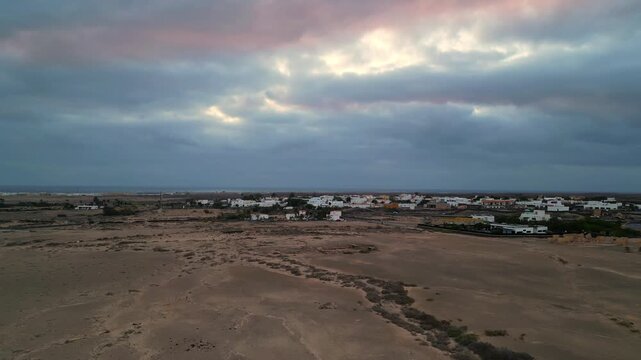 Aerial view of the coastal village of El Cotillo with white buildings and arid landscape under a dramatic cloudy sky in El Cotillo, Canary Islands, Spain.