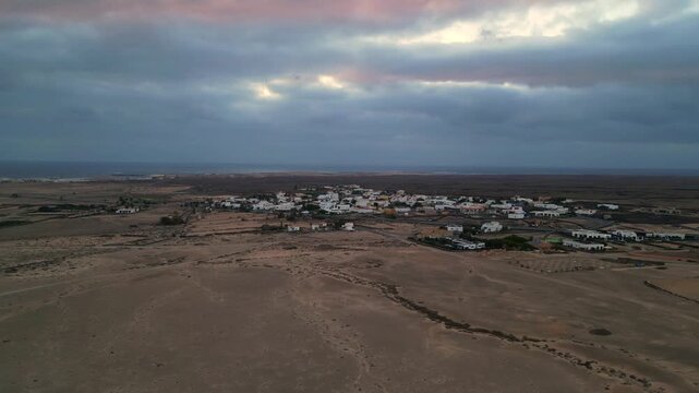 Aerial view of El Cotillo village surrounded by arid volcanic landscape under a dramatic cloudy sky in El Cotillo, Canary Islands, Spain.