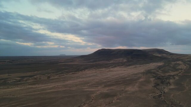 Aerial view of the arid volcanic landscape near El Cotillo with rolling hills and a cloudy sky at dusk in El Cotillo, Canary Islands, Spain.