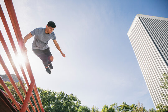 Young man jumping over railing performing parkour against clear sky in city