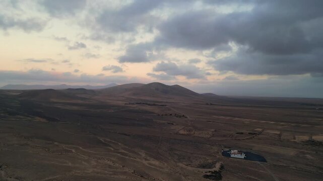 Aerial view of the volcanic landscape and rolling hills under a cloudy sky at sunset in El Cotillo, Canary Islands, Spain.