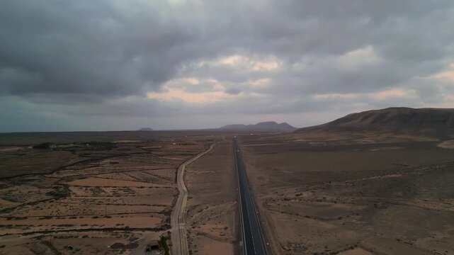 Aerial view of a long straight road cutting through the arid volcanic landscape of El Cotillo, Canary Islands, Spain.