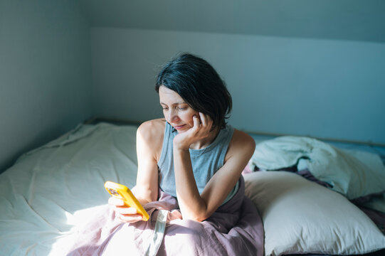 Woman sitting in bed using smartphone in the morning