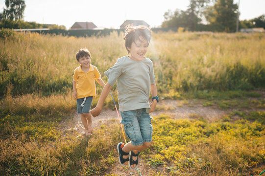 A boy and his brother run and jump rope in a sunny countryside yard