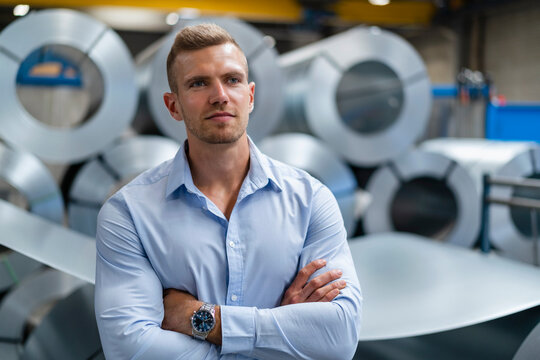 Confident young businessman looking away while standing with arms crossed at factory