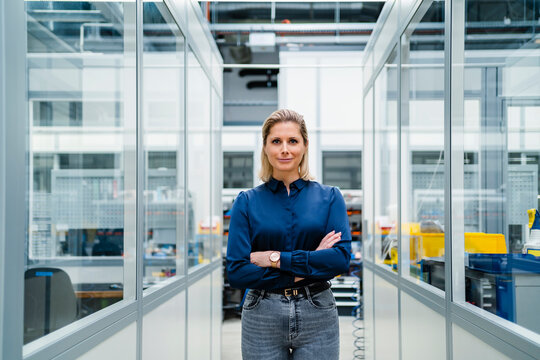 Confident businesswoman with arms crossed standing between cabins in factory