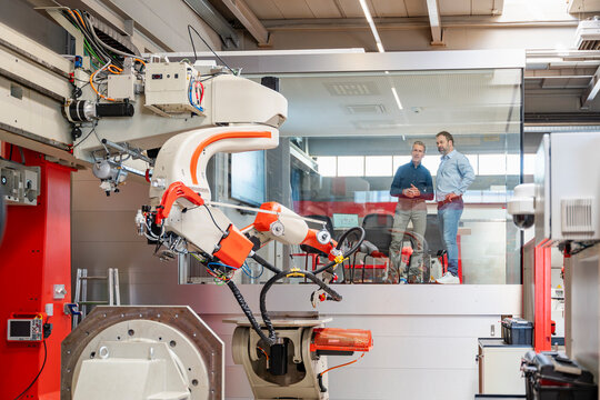 Men observe an industrial robot from a glass office