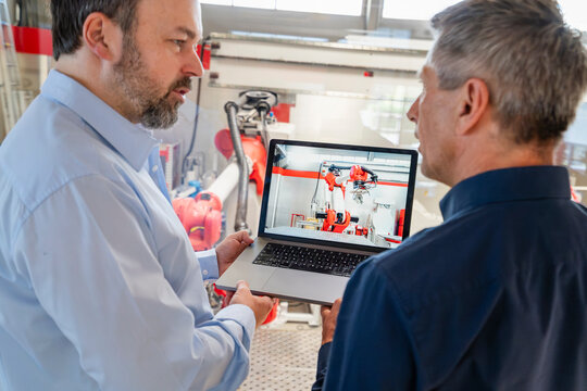 Engineer shows industrial robot on laptop to manager in factory
