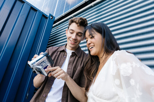 Happy man and woman watch a video on a camcorder outdoors