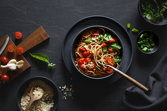 Bowl of vegan wholemeal spelt spaghetti with tomatoes, basil, scallion and cashew Parmesan