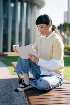 Smiling woman sitting outdoors using digital tablet on sunny day
