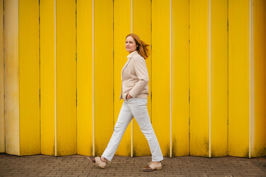 Confident businesswoman walking outdoors by yellow wall