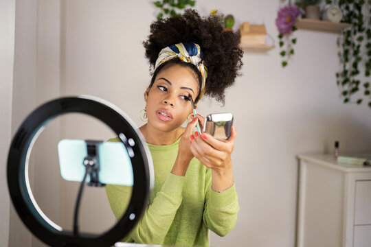 Female influencer giving make-up tutorial through vlogging at home