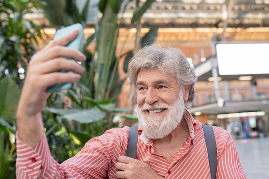 Happy white bearded man taking selfie through smart phone at station