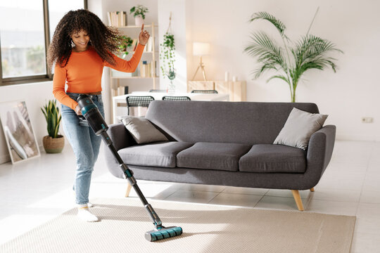 Smiling young woman with vacuum cleaner dancing in living room at home