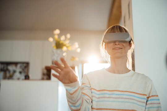 Smiling woman with virtual reality headset gesturing at home