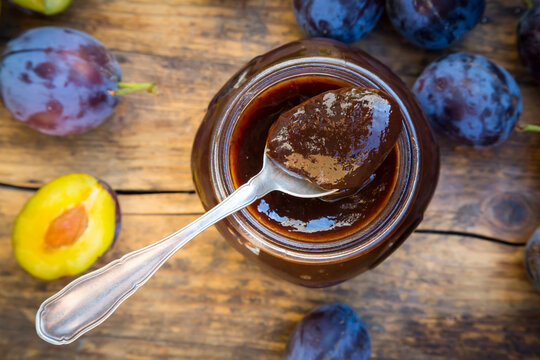 Tea spoon of plum jam on preserving jar and plums on wood