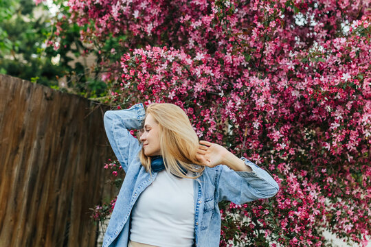 A blonde woman enjoys music near a blooming pink tree