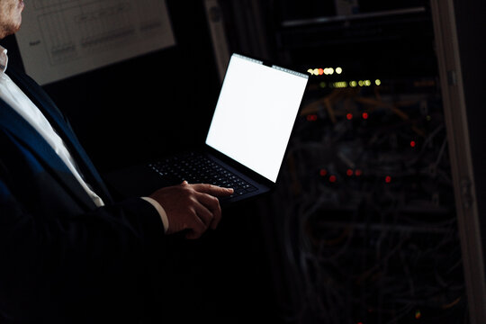 Male administrator holds a blank laptop near an IT cabinet