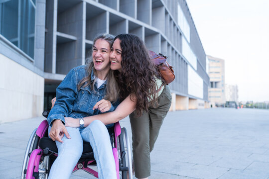 Woman hugs her laughing friend in a wheelchair outdoors