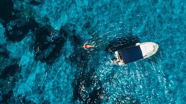 Woman swims in clear blue sea near a boat in Sardinia Italy