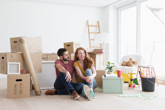 Young couple in new flat with cardboard boxes, sitting on floor