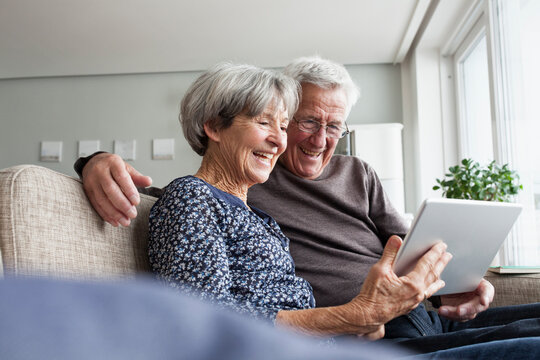 Happy senior couple sitting on the couch in the living room using digital tablet