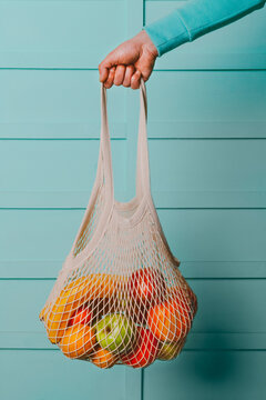 Arm of man holding reusable cotton mesh bag with fresh fruits