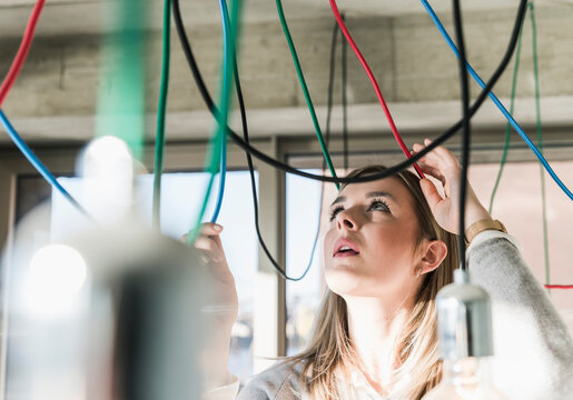 Young businesswoman in office examining cables at light bulbs