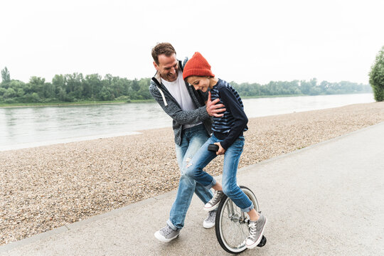 Happy father supporting son on unicycle at the riverside