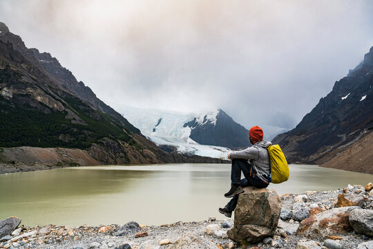 Hiker sitting on rock looking at glacier lake in Patagonia